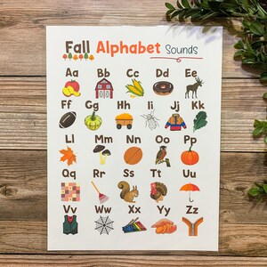 May include: A colorful alphabet chart with fall-themed illustrations for each letter. The chart includes images like an apple, a barn, corn, a donut, a moose, a football, a pumpkin, a wagon, a bug, a jacket, kale, a maple leaf, mushrooms, a basketball, an owl, a pumpkin, a checkerboard, a rake, a squirrel, a turkey, an umbrella, a vest, a spider web, xylophone, sweet potatoes, and a zipper.