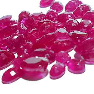 May include: A collection of faceted, deep red gemstones, possibly rubies, scattered against a white background. The gems vary in size and shape, with multiple facets catching the light, creating a sparkling effect. The overall theme is jewelry and gemstones.