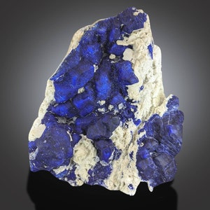 Op de afbeelding: Een opvallend exemplaar van azuriet, een diepblauw mineraal. De azuriet is vermengd met een lichtere, gebroken witte matrix, wat een aantrekkelijk contrast creëert. De rotsformatie heeft een ruw, getextureerd oppervlak.