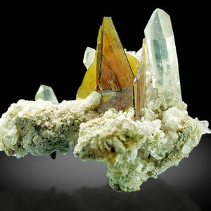 May include: A cluster of crystals featuring a central, multi-faceted, brown and yellow crystal formation. Clear, pointed quartz crystals and smaller, white crystals are also present. The crystals rest on a base of light green and white mineral deposits, against a black background.