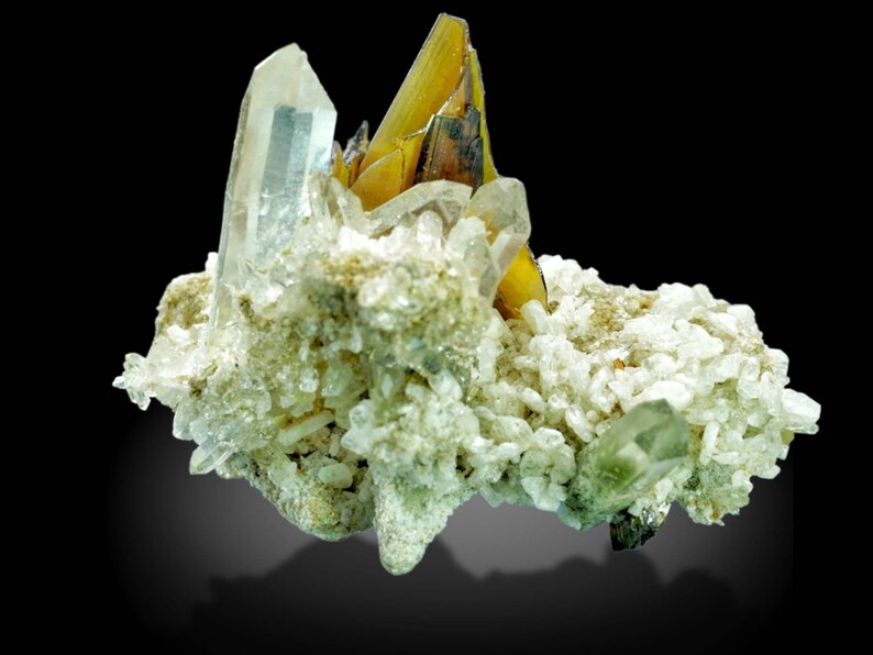 May include: A cluster of natural crystals, featuring a large, clear quartz crystal alongside golden-yellow and clear crystals. The crystals are set against a backdrop of smaller, white and light green crystals, creating a striking contrast. The background is black.