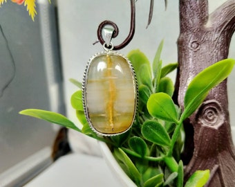 May include: A silver pendant with a rectangular, rounded gemstone. The gemstone is a translucent, light yellow color with golden-yellow inclusions. The pendant has a silver rope-like border and a silver bail.