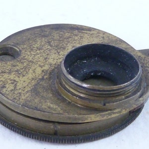 May include: A brass telescope lens cap with a black rubber ring around the opening. The cap has a worn, aged appearance.