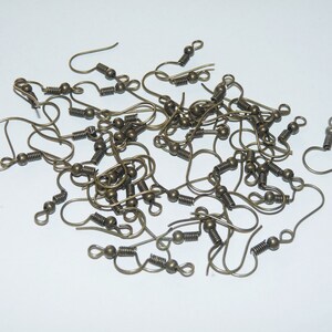 May include: A pile of gold-toned earring hooks with spring closures. The hooks are made of metal and have a small ball at the end.