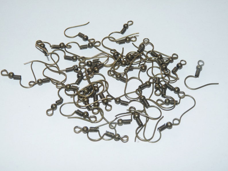 May include: A pile of gold-toned earring hooks with spring closures. The hooks are made of metal and have a small ball at the end.