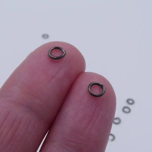 May include: Two silver jump rings, each about 1/2 inch in diameter, are held between two fingers.