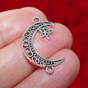 Puede incluir: Encanto de plata con forma de luna creciente con una estrella en su interior. La luna está decorada con un patrón circular. El encanto tiene dos anillos de salto para sujetarlo a joyas.