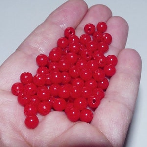 Peut inclure: Un grand tas de perles rondes en plastique rouge vif. Les perles sont lisses et brillantes.
