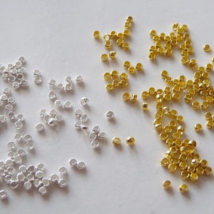 Puede incluir: Una imagen de primer plano de dos pilas de pequeños anillos de salto redondos de metal. Una pila es dorada y la otra es plateada.