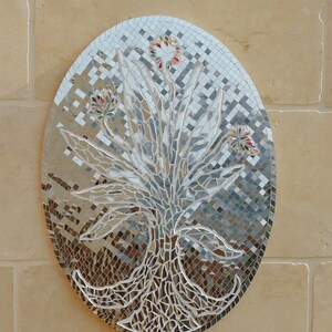 May include: An oval-shaped mosaic art piece featuring a stylized tree design. The mosaic is made of small, reflective mirrored tiles, with colorful accents in the flowers. The artwork is mounted on a light beige wall.