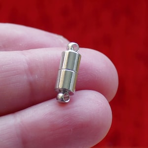 May include: Silver magnetic clasp for jewelry making. The clasp is cylindrical and has a smooth, polished finish.