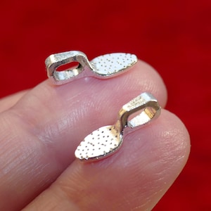 Puede incluir: Dos abalorios de metal plateado en forma de zapato con una superficie texturizada. Los abalorios tienen un bucle en la parte superior para sujetarlos a una pulsera o un collar.