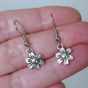 May include: A pair of silver dangle earrings with a small flower charm. The earrings have a simple design and are perfect for everyday wear.