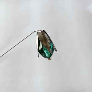 Könnte beinhalten: Ein silberner Blumenstiel mit einem grünen Kristallblumenkopf.