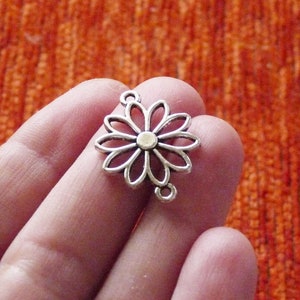May include: Silver-toned metal flower charm with a circular centre and openwork design. The charm has two loops on the back for attaching to jewellery or other crafts.