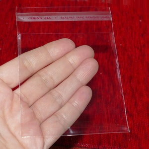 Może przedstawiać: Przezroczysty plastikowy woreczek z czerwoną etykietą z napisem "# CHENG JIA # SEALING TAPE REMOVE LINER".