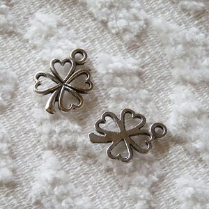 May include: Two silver four-leaf clover charms with a loop for attaching to a necklace or bracelet.
