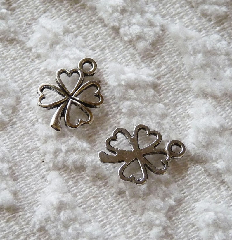 May include: Two silver four-leaf clover charms with a loop for attaching to a necklace or bracelet.