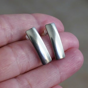 Puede incluir: Un par de pendientes de barra de plata. Los pendientes son simples y elegantes, con un acabado pulido.