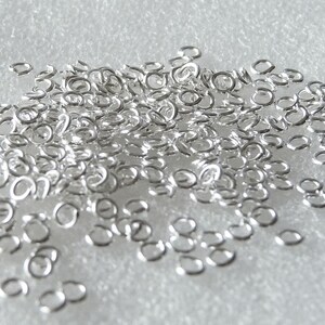 May include: A large pile of silver jump rings, a type of jewellery finding used for connecting chains, cords, and other jewellery components.