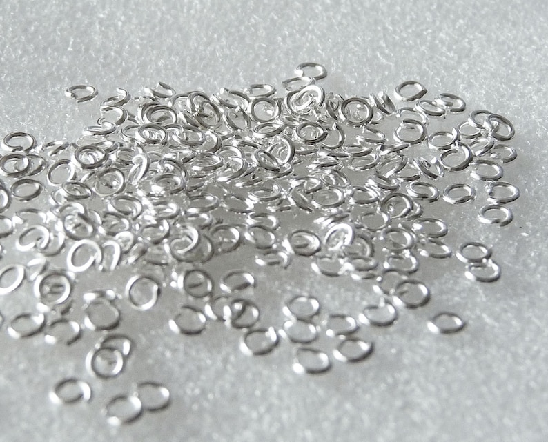 May include: A large pile of silver jump rings, a type of jewellery finding used for connecting chains, cords, and other jewellery components.