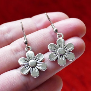 May include: A pair of silver dangle earrings featuring a flower design. The earrings have a simple hook closure.