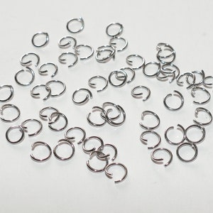 May include: A large quantity of silver jump rings, a type of jewelry finding used for connecting chains, cords, and other jewelry components.