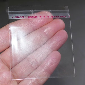 Puede incluir: Bolsa de pl&aacute;stico transparente con un sello rojo que dice "OKER BRAND SEALING TAPE".