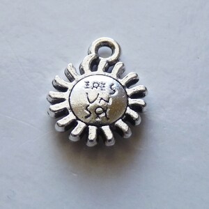 Könnte beinhalten: Silberner Anhänger in Form einer Sonne mit einem Strichmännchen-Design im Inneren. Die Sonne hat 16 Strahlen.
