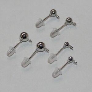 May include: Six pairs of silver earring posts with clear silicone backs. The earring posts have a small ball at the top and a loop at the bottom.