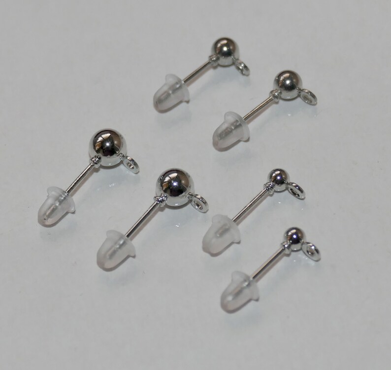May include: Six pairs of silver earring posts with clear silicone backs. The earring posts have a small ball at the top and a loop at the bottom.