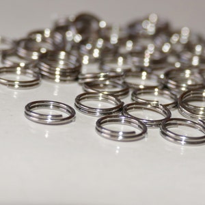 Puede incluir: Primer plano de un mont&oacute;n de anillos de salto plateados. Los anillos son peque&ntilde;os y redondos, y todos son del mismo tama&ntilde;o. Son perfectos para la elaboraci&oacute;n de joyas u otras manualidades.