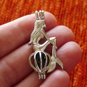 Peut inclure: Charme de sirène en argent avec une perle de verre bleue à l'intérieur. La sirène est assise sur un rocher avec sa queue enroulée autour d'elle.