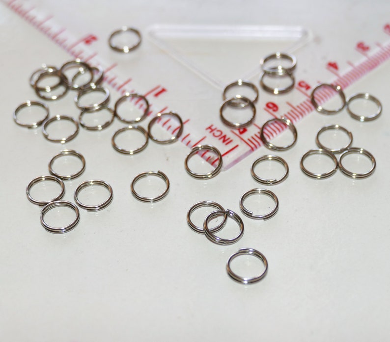 Puede incluir: Primer plano de un mont&oacute;n de anillos de salto plateados. Los anillos son de varios tama&ntilde;os y est&aacute;n dispersos sobre una superficie blanca.