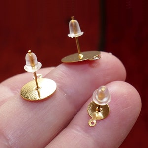 Puede incluir: Tres postes de pendientes de oro con respaldos de goma transparente. Los postes son redondos y tienen un pequeño bucle en la parte inferior.