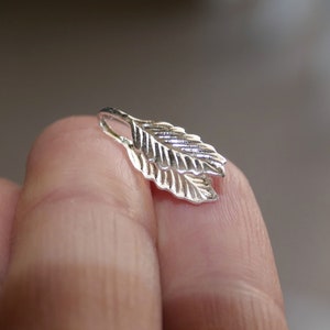 Op de afbeelding: Zilveren bladhanger met een gedetailleerd ontwerp. De hanger is gevormd als twee overlappende bladeren.