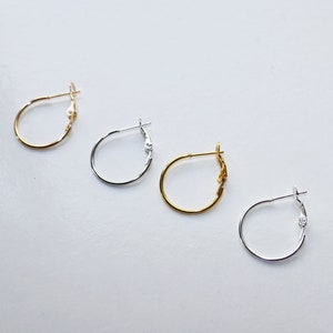 Puede incluir: Cuatro pares de pendientes de aro en diferentes estilos. Dos pares son de plata, uno es de oro y uno es de oro con un diseño decorativo.