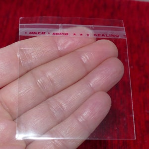 Puede incluir: Bolsa de pl&aacute;stico transparente con una banda de sellado t&eacute;rmico roja que dice "OKER BRAND *** SEALING".
