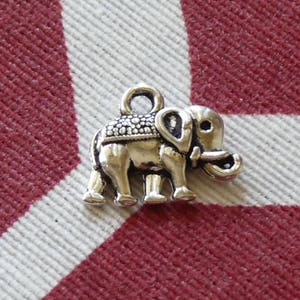 K&ouml;nnte beinhalten: Ein silberner Anh&auml;nger in Form eines Elefanten. Der Elefant hat eine strukturierte Oberfl&auml;che und eine kleine Schlaufe oben zum Anbringen an einer Halskette oder einem Armband.