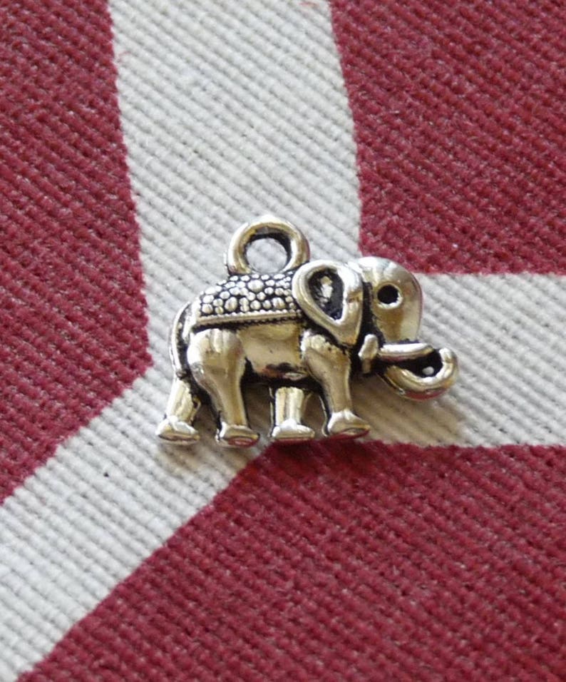 K&ouml;nnte beinhalten: Ein silberner Anh&auml;nger in Form eines Elefanten. Der Elefant hat eine strukturierte Oberfl&auml;che und eine kleine Schlaufe oben zum Anbringen an einer Halskette oder einem Armband.