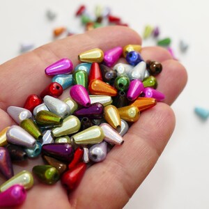 以下が含まれることがあります： 赤、ピンク、金、緑、銀などのメタリックカラーの、しずく型のビーズのコレクション。これらのビーズは、ジュエリー作りやその他のクラフトプロジェクトに適しています。