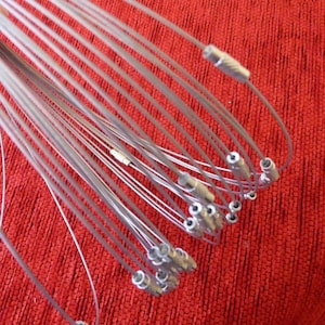 Op de afbeelding: Een bundel zilverkleurige metalen kabelbinders met kleine plastic uiteinden. De kabelbinders zijn spiraalvormig op een rood oppervlak gerangschikt.