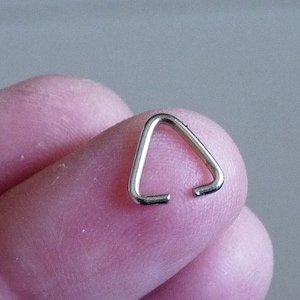Può includere: Un anello di salto triangolare in argento, un piccolo anello di metallo utilizzato per collegare i componenti dei gioielli.