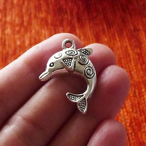 Puede incluir: Encanto de delfín plateado con un patrón de espiral detallado. El encanto tiene un bucle en la parte superior para sujetarlo a un collar o pulsera.