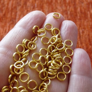 Puede incluir: Una mano sosteniendo una gran cantidad de peque&ntilde;os anillos de salto dorados. Los anillos son todos del mismo tama&ntilde;o y est&aacute;n dispuestos en un patr&oacute;n aleatorio.