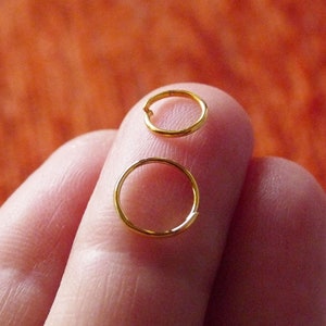 Puede incluir: Dos pendientes de aro dorados de diferentes tamaños. El aro más grande está a la izquierda y el más pequeño a la derecha.