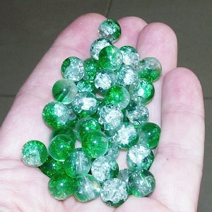 Pode incluir: Uma coleção de contas de vidro verde com manchas prateadas. As contas são redondas e têm uma aparência translúcida.