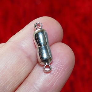 May include: Silver magnetic clasp for jewellery making. The clasp is shaped like a peanut and has two loops on each end.
