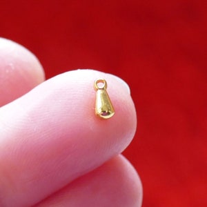 May include: A small, gold-colored pendant shaped like a teardrop. The pendant has a loop at the top for attaching to a chain or cord.