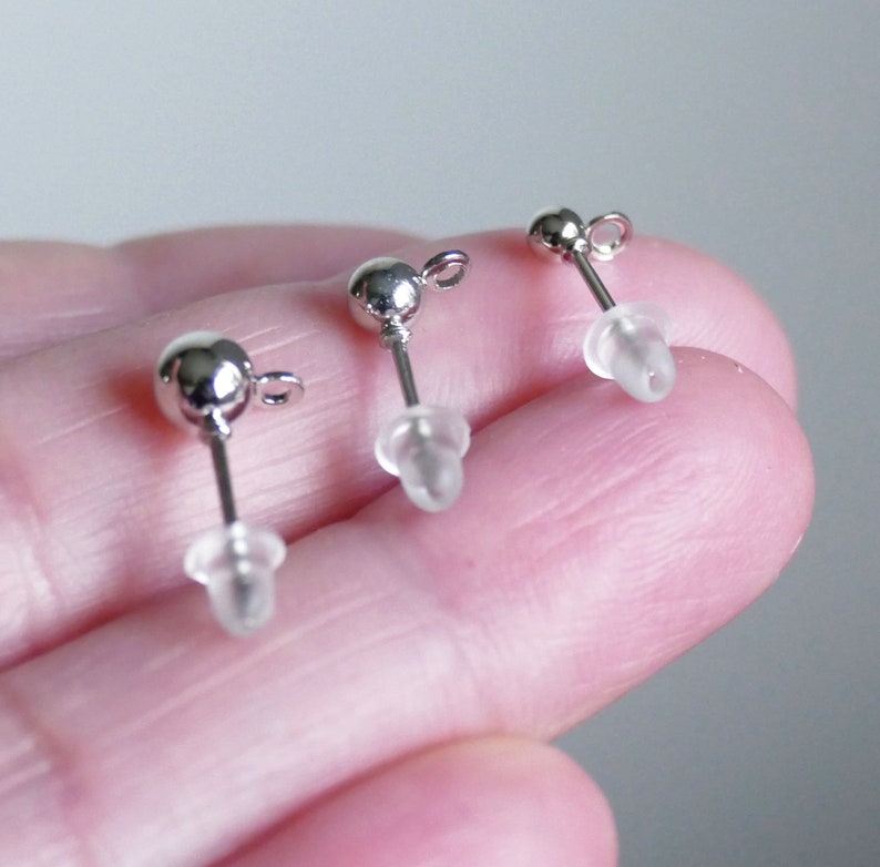 May include: Three silver earring posts with clear rubber backs. The posts are round and have a small loop at the top.